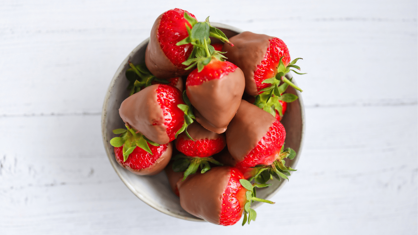 A deliciously tempting bowl of chocolate-covered strawberries sits in the middle of a table.