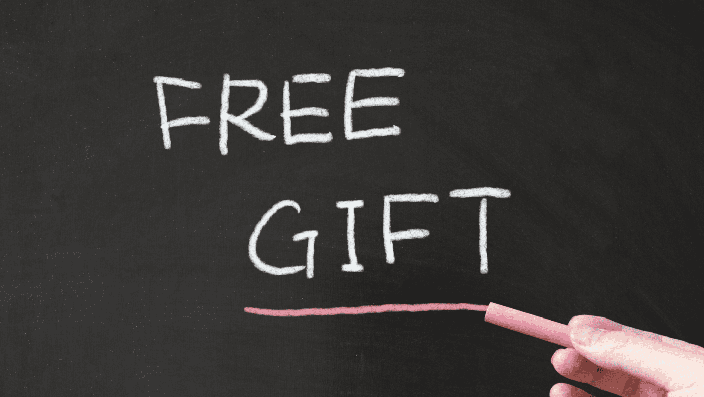 A person underlines the words "FREE GIFT" in pink chalk on a black board.